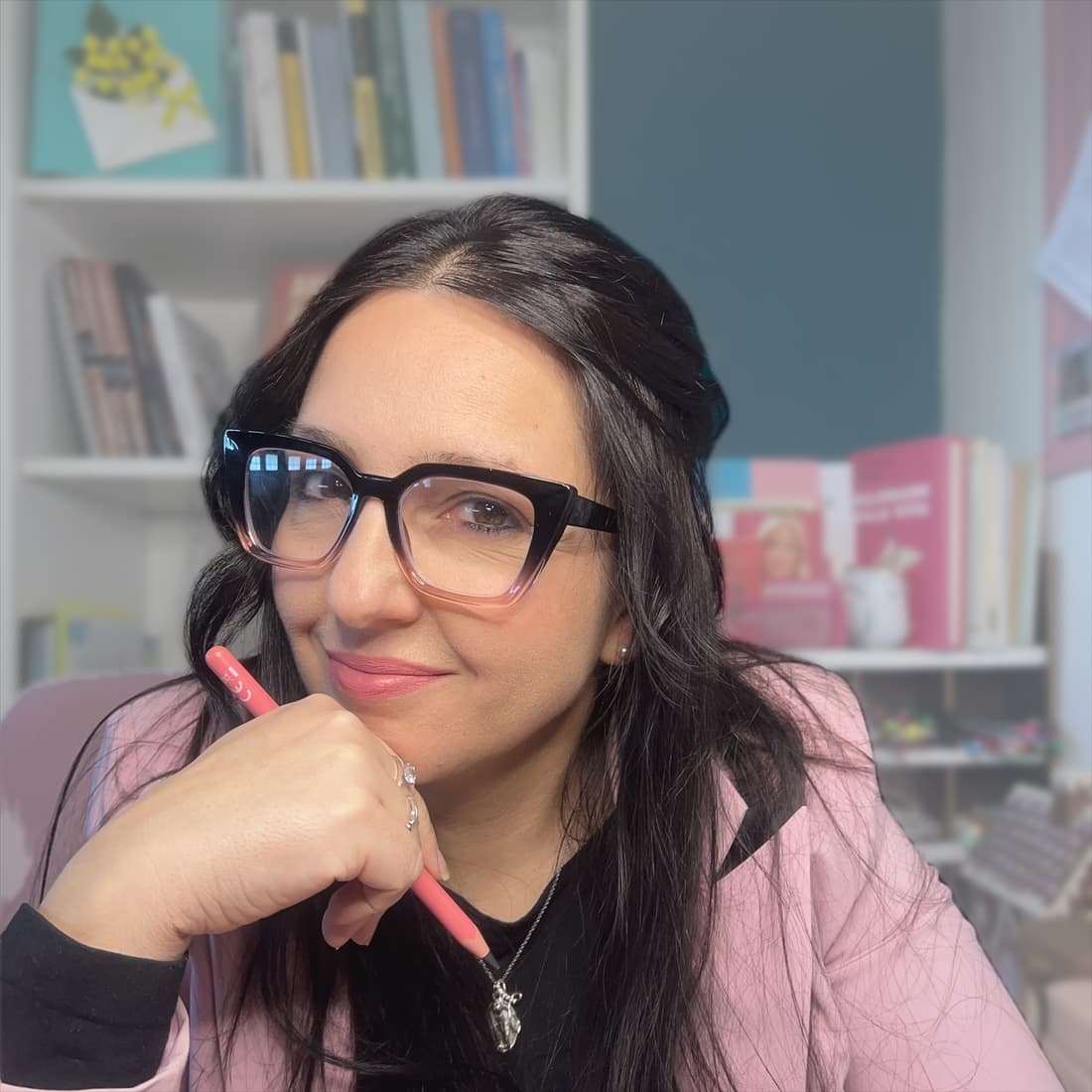 Patrizia, occhiali scuri e giacca rosa, il mento appoggiato alla mano che tiene una matita
